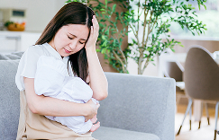赤ちゃんを抱えながら悩んでいる女性の写真